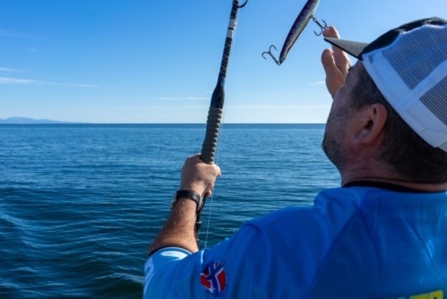 man on the deck of private fishing boat about to cast his fishing rod into the sea.